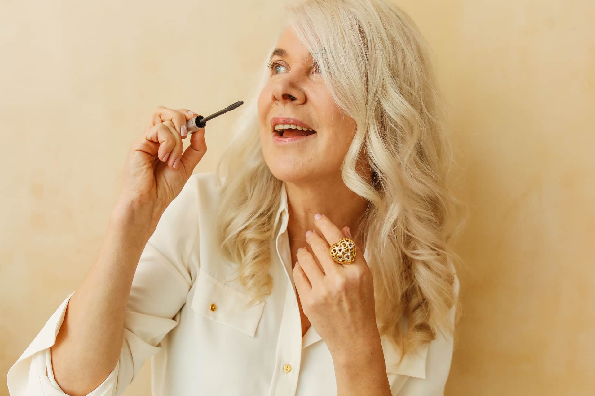 A smiling senior woman applying mascara in a bright room
